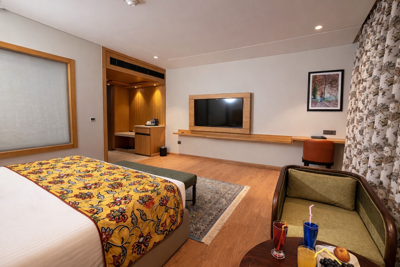 A hotel room with a bed, a desk, a television, a chair, and a small table with a drink and a plate of food.