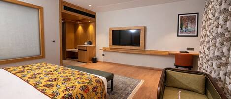 A hotel room with a bed, a desk, a television, a chair, and a small table with a drink and a plate of food.