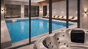 Una piscina interior moderna con paredes de vidrio transparente, sillas de descanso y un jacuzzi.
