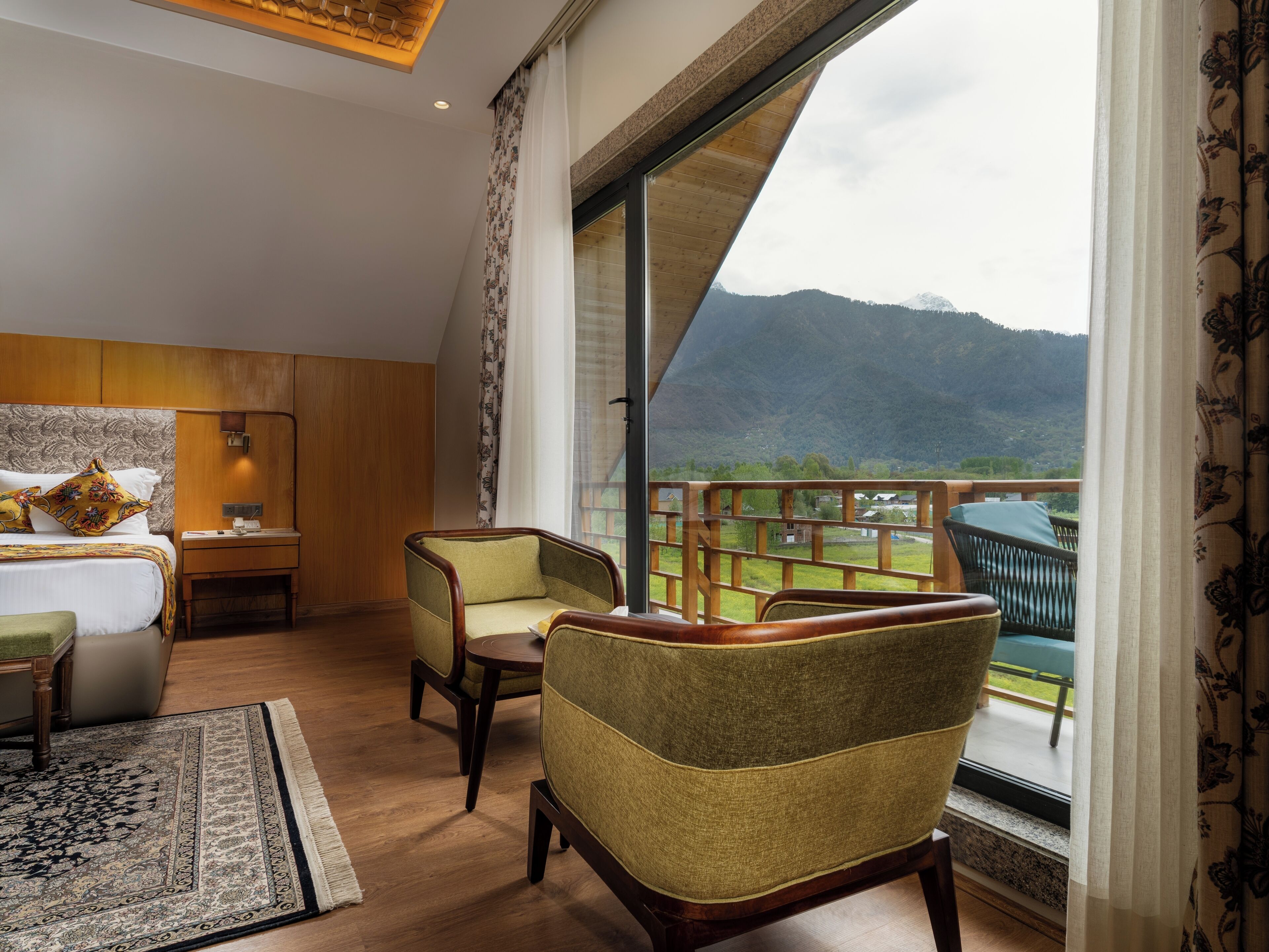 A hotel room with a large window, a bed, a desk, and two chairs.
