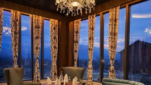 Comedor con candelabro, cortinas estampadas y vistas a un edificio a través de amplios ventanales.