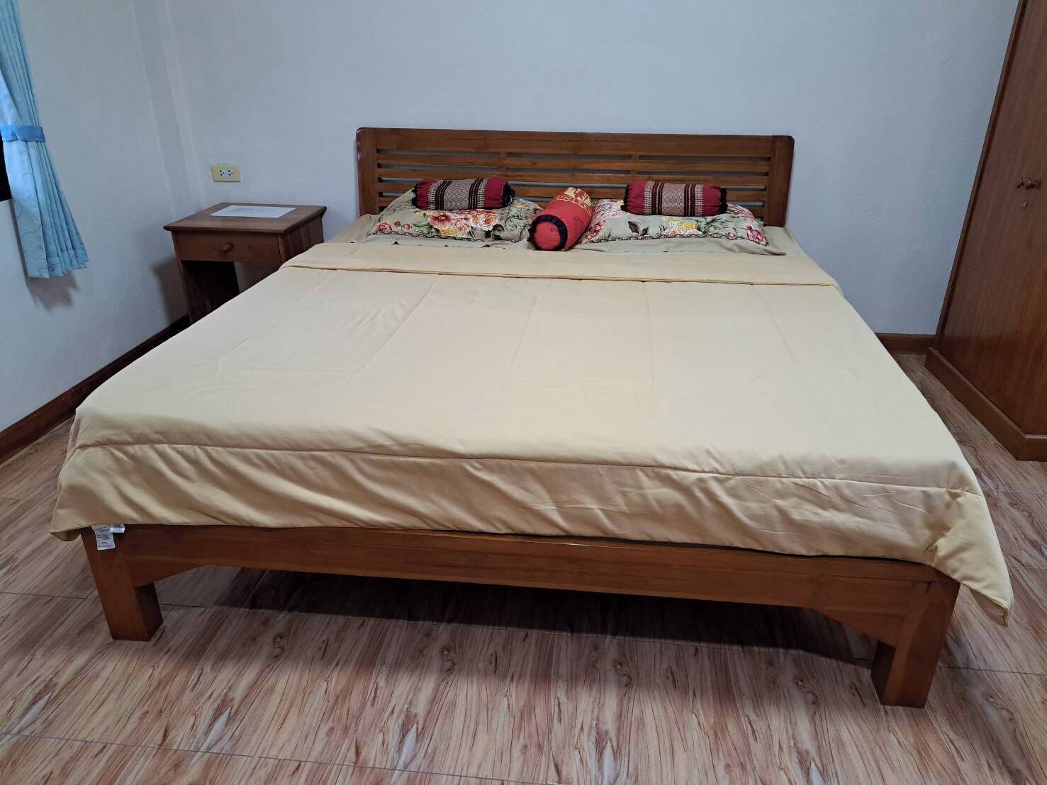 Cama com estrutura de madeira, colchão bege e almofadas estampadas.
