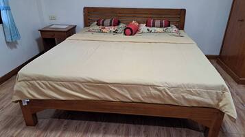 Cama com estrutura de madeira, colchão bege e almofadas estampadas.