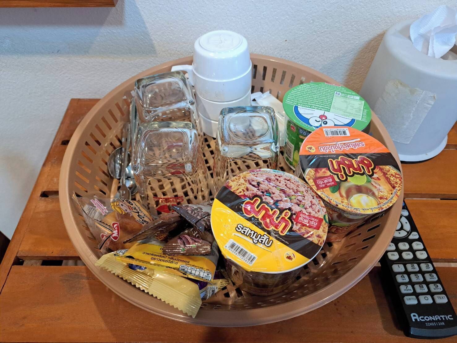 Una cesta con diversos alimentos, un control remoto y una botella de agua.