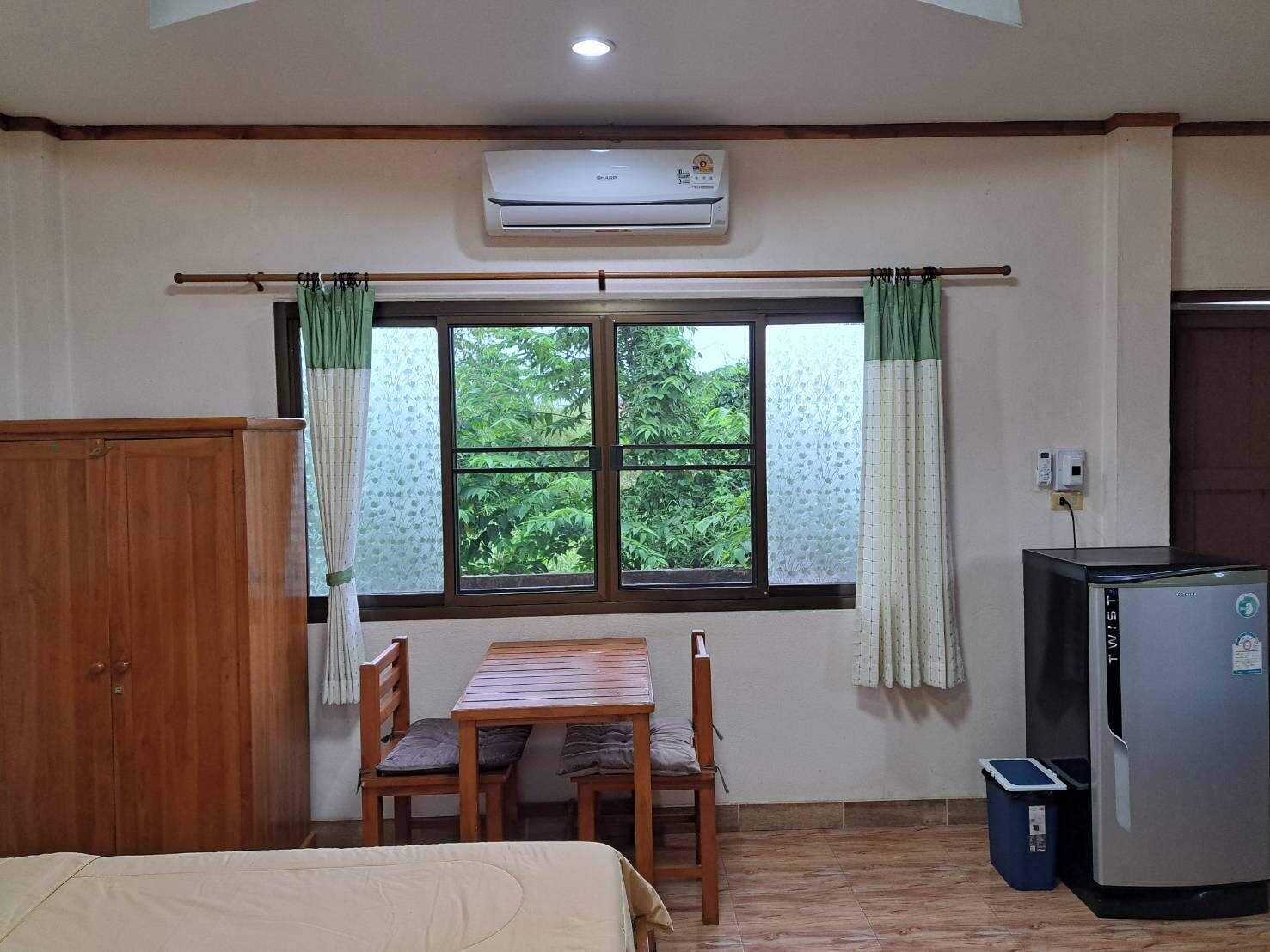 Une chambre comprenant un lit, une table avec des chaises, une fenêtre avec des rideaux, un climatiseur et un réfrigérateur.
