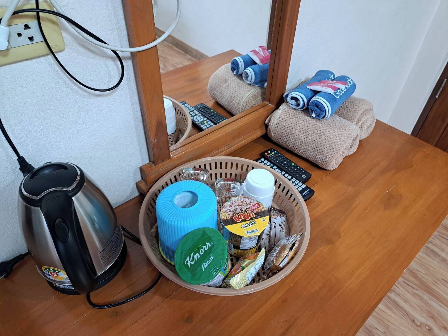 Una habitación con una mesa de madera, una cesta de aperitivos, un hervidor y un control remoto.