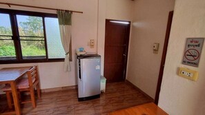 A compact room with a wooden table and chairs, a refrigerator, a window with curtains, a door, and a no-smoking sign. - Sinsawat Resort (Uttaradit)