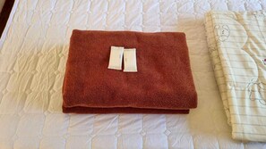 A neatly folded brown towel on a bed with a white quilted bedspread and a striped blanket with a bear design. - Sinsawat Resort (Uttaradit)