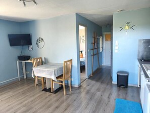 Ein Zimmer mit Esstisch, Stühlen, Fernseher, einer Leiter und einer Wanduhr.