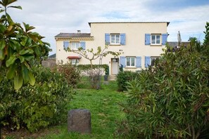 Ein zweistöckiges Haus mit Garten, einem Stein in der Mitte und blauem Himmel.