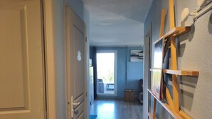 Un couloir avec une porte en bois, un porte-manteau en bois et une vue sur une pièce dotée d’une fenêtre.
