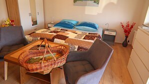 Une chambre à coucher comprenant un lit, des tables de chevet, une commode, une chaise, une table avec un panier et un tableau accroché au mur.