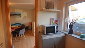 Une cuisine compacte avec un four à micro-ondes posé sur le plan de travail, un coin repas avec une table et des chaises, et une fenêtre donnant sur la rue.