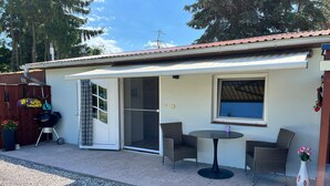 Un espace patio avec une table et des chaises, une porte-fenêtre coulissante et un petit jardin fleuri.