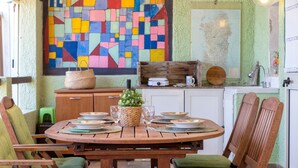 Ein Holztisch mit Stühlen, eine Wand mit Mosaiken und eine Küchenzeile mit Küchenutensilien.