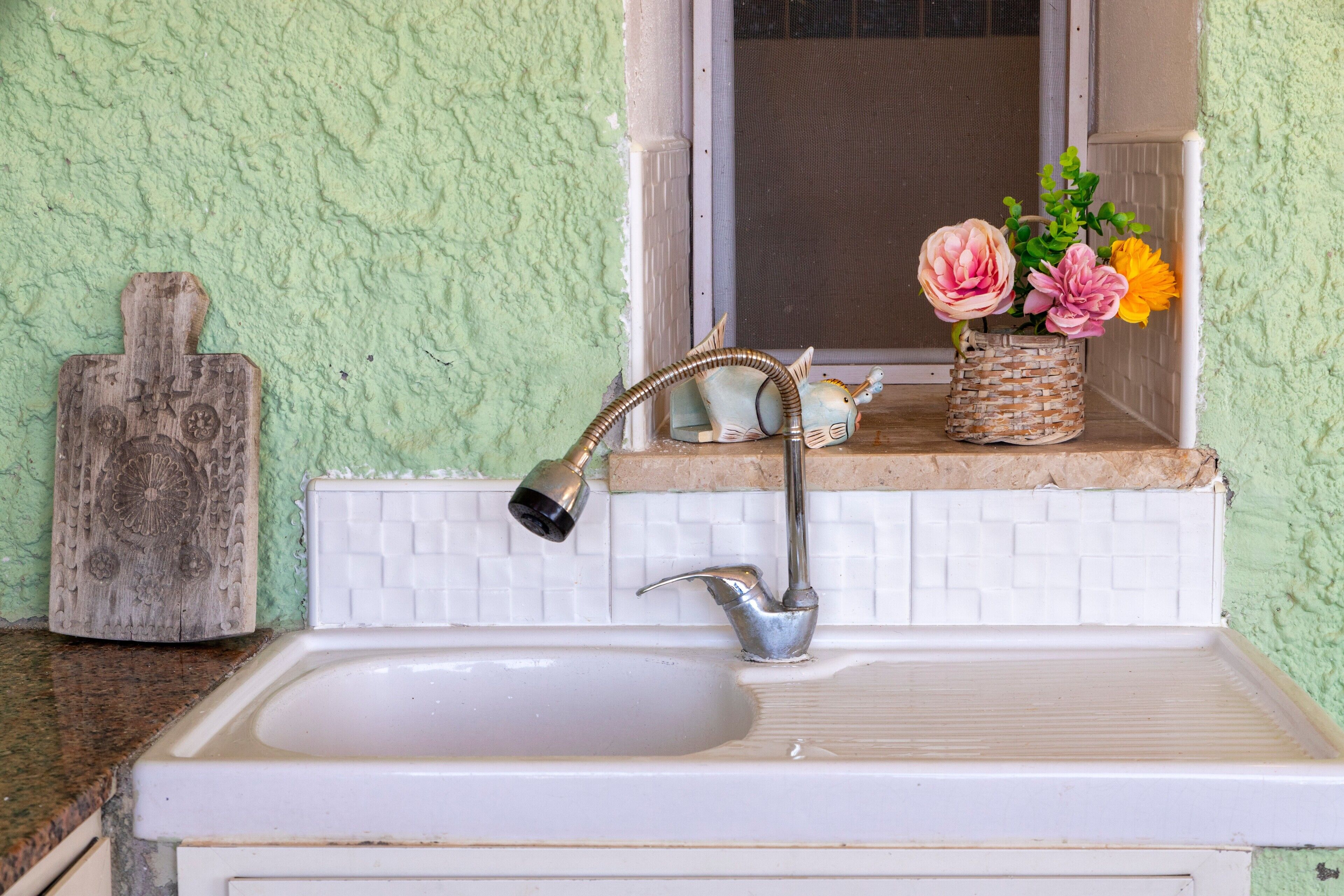 A kitchen sink with a faucet, a window with a view, and a basket of flowers on the window sill.