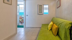 Ein Zimmer mit einem grünen Sofa, einer zur Balkonführenden Tür und einem gerahmten Bild an der Wand.