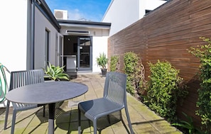 Een terras met een tafel en twee stoelen, een houten hek en wat groen.