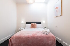 Een netjes ingerichte hotelkamer met een bed, twee nachtkastjes, een lamp, een ingelijste foto en een stapel handdoeken.