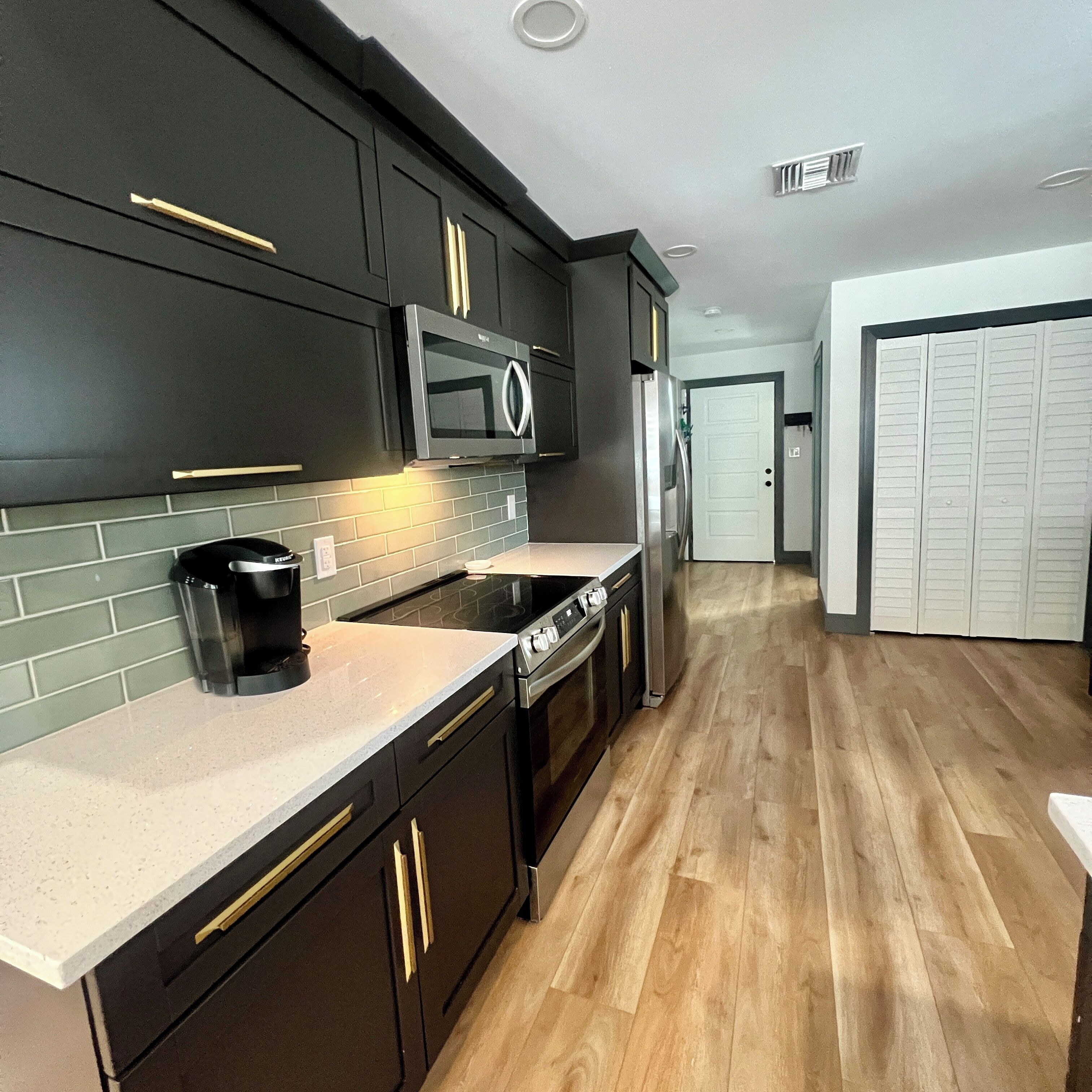 A modern kitchen with dark cabinetry, a microwave, a stove, and a refrigerator.