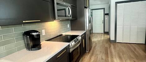 A modern kitchen with dark cabinetry, a microwave, a stove, and a refrigerator.