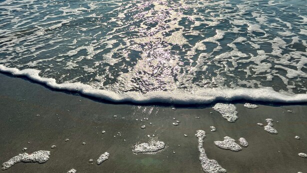 Een strand met helder water, golven en een stralende zon.