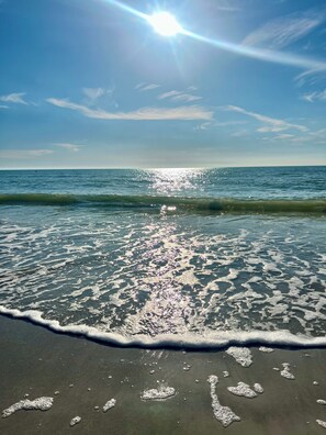 Ein Strand mit klarem Wasser, Wellen und strahlender Sonne.