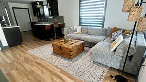 Een moderne woonkamer met een houten salontafel, een grijze bank en een keuken in de achtergrond.