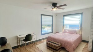 Een slaapkamer met een bed, een bureau, een stoel, een plafondventilator en een raam.