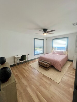 Ein Schlafzimmer mit einem Bett, einem Schreibtisch, einem Stuhl, einem Deckenventilator und einem Fenster.