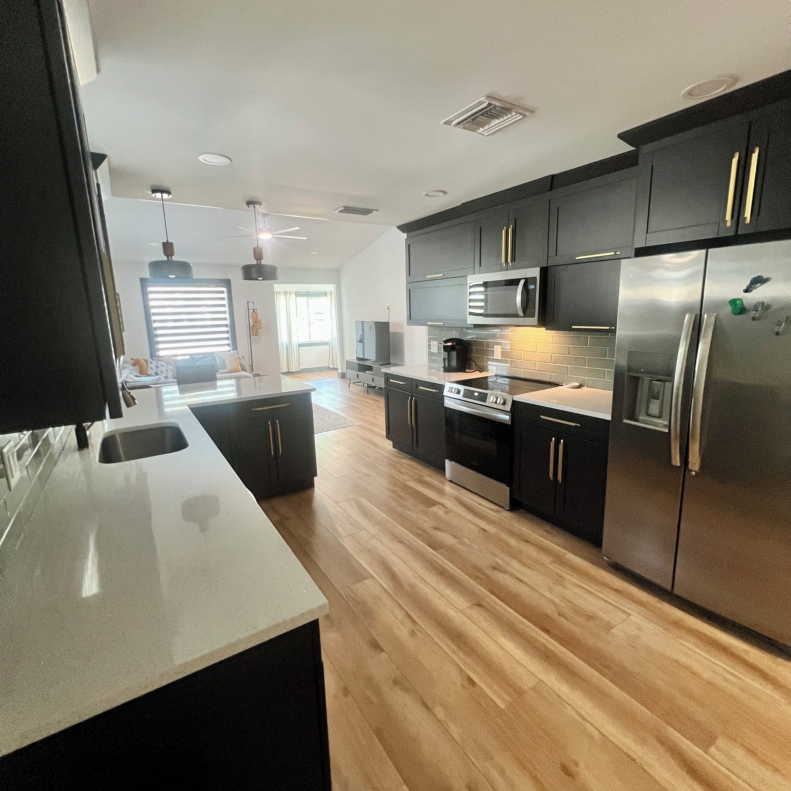 A modern kitchen with dark cabinets, stainless steel appliances, and a wooden floor.