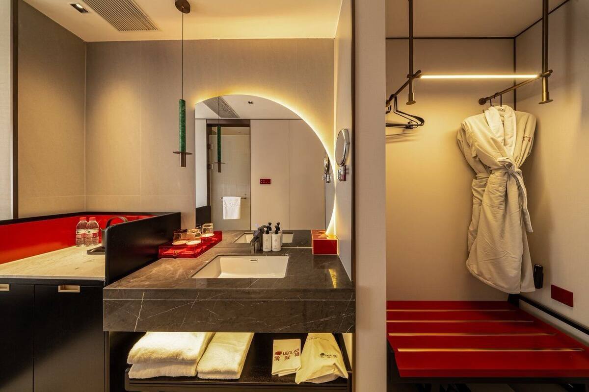 A modern bathroom with a large mirror, a sink, a robe hanging, and a towel rack.
