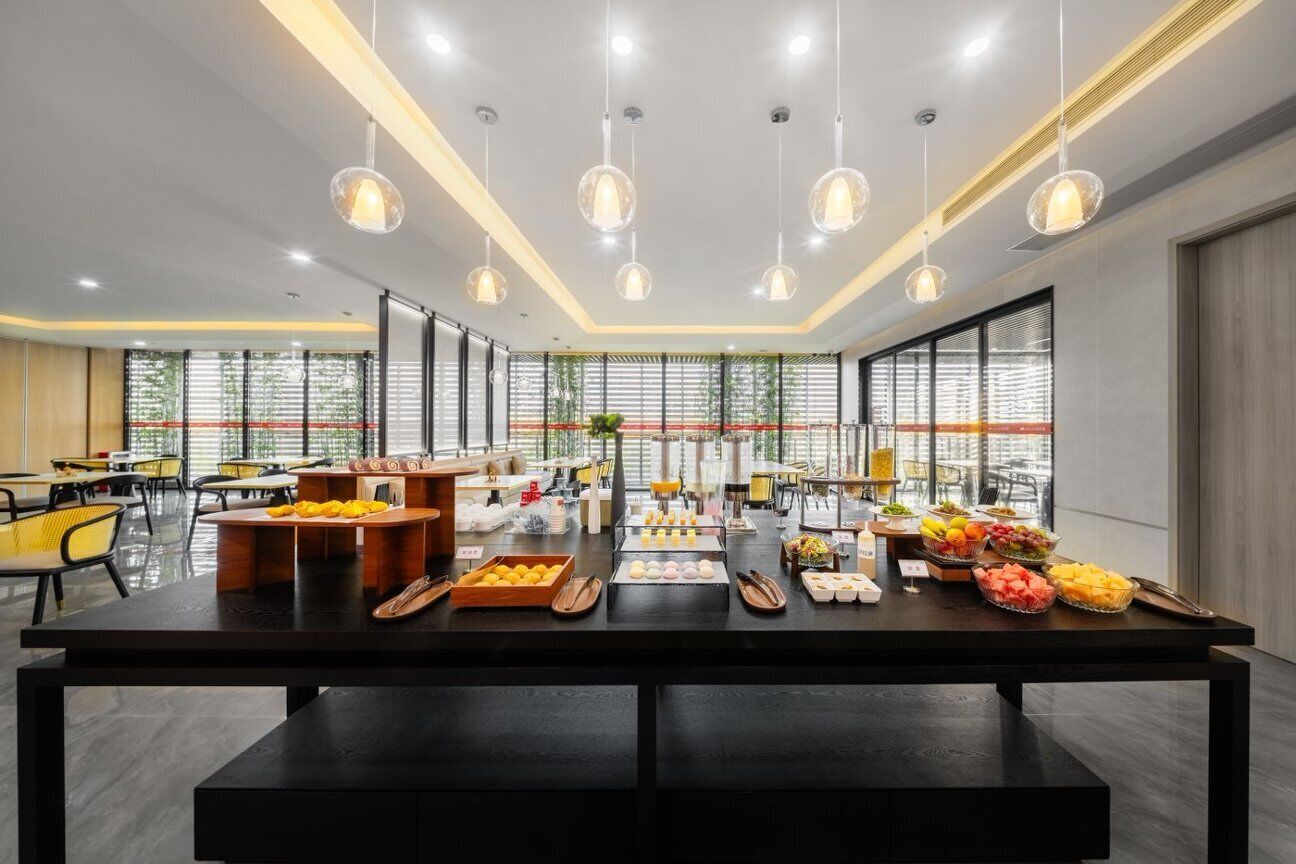 A modern dining area with a long table, multiple hanging pendant lights, and a view through large windows.