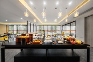 Un espace de salle à manger moderne, avec une longue table, de nombreuses suspensions et une vue dégagée sur l’extérieur grâce à de grandes fenêtres.