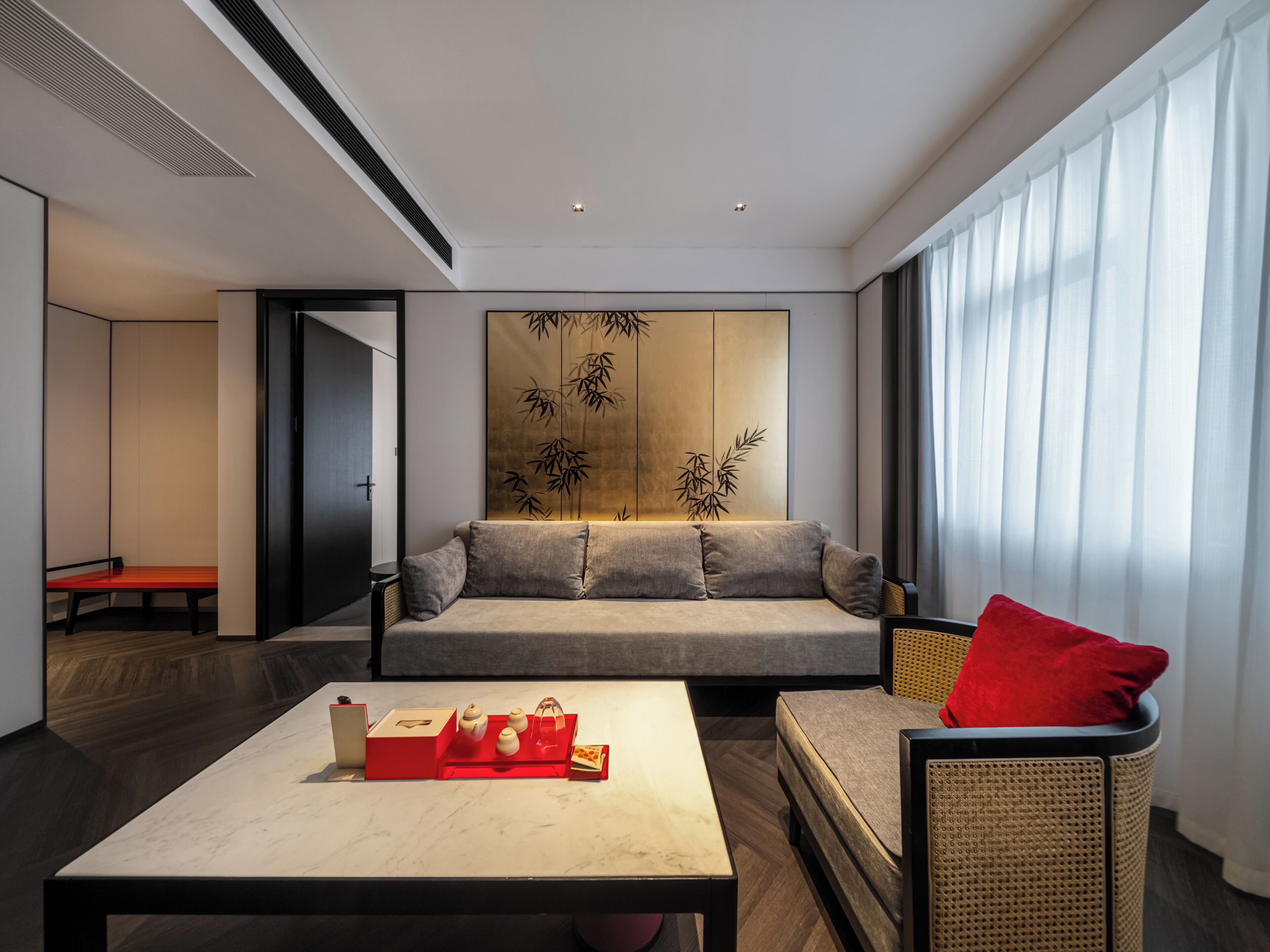 A modern hotel room with a sofa, a coffee table, a wicker chair, and a wall with a bamboo design.
