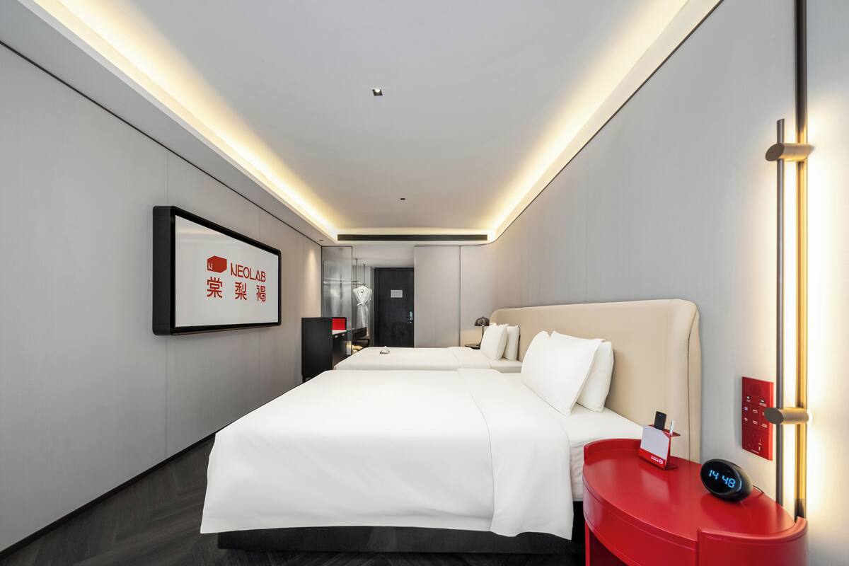 A modern hotel room with a large bed, a red side table with a clock, and a framed sign on the wall.