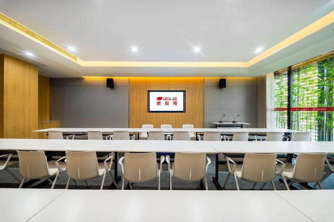 Une salle de conférence avec une longue table et des chaises, un écran affichant du texte et une fenêtre donnant sur un espace verdoyant.