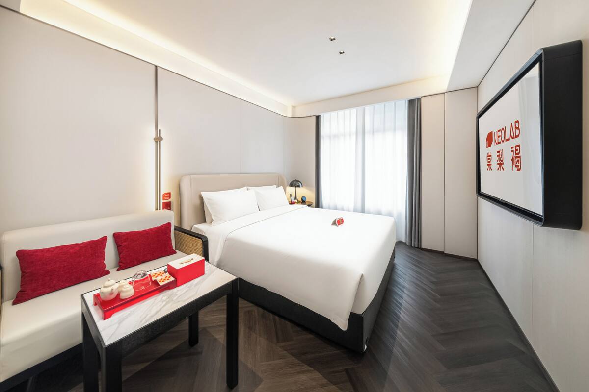 A modern hotel room with a bed, a sofa, a coffee table, and a TV screen displaying text.