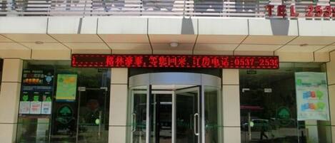 A hotel entrance with a glass door, a digital display above the door, and a brick-paved ground.