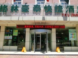 A hotel entrance with a glass door, a digital display above the door, and a brick-paved ground.
