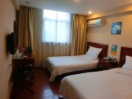 A hotel room with two beds, a desk with a chair, a television, and an air conditioning unit.