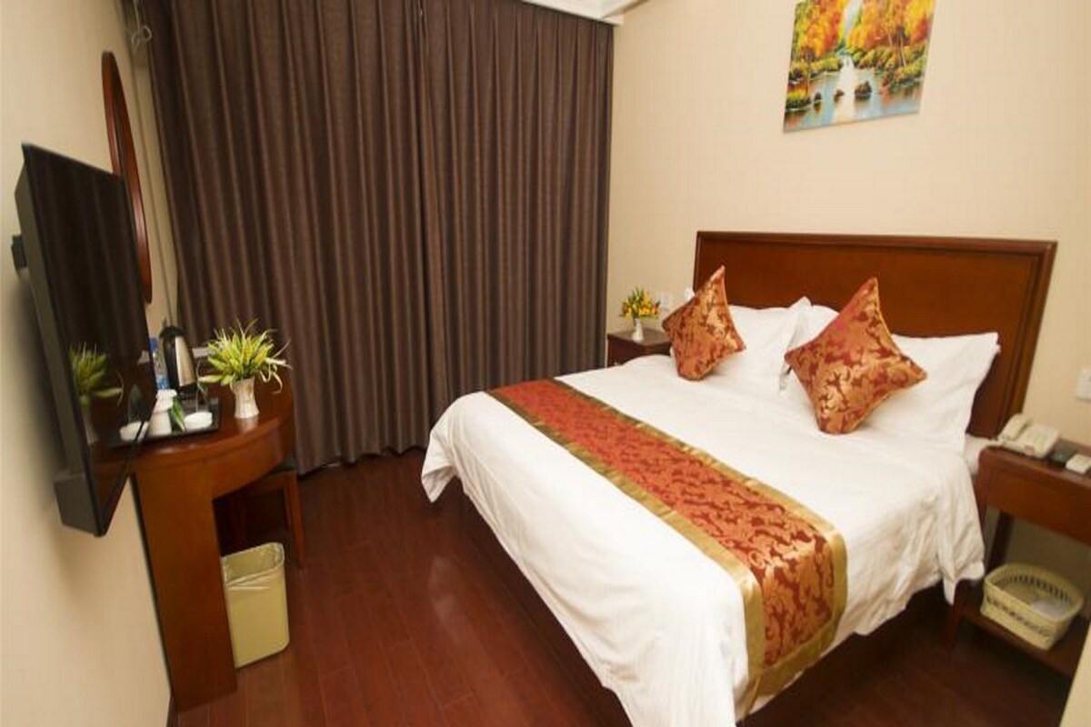 A hotel room with a bed, a desk with a telephone, a television, and a window with curtains.