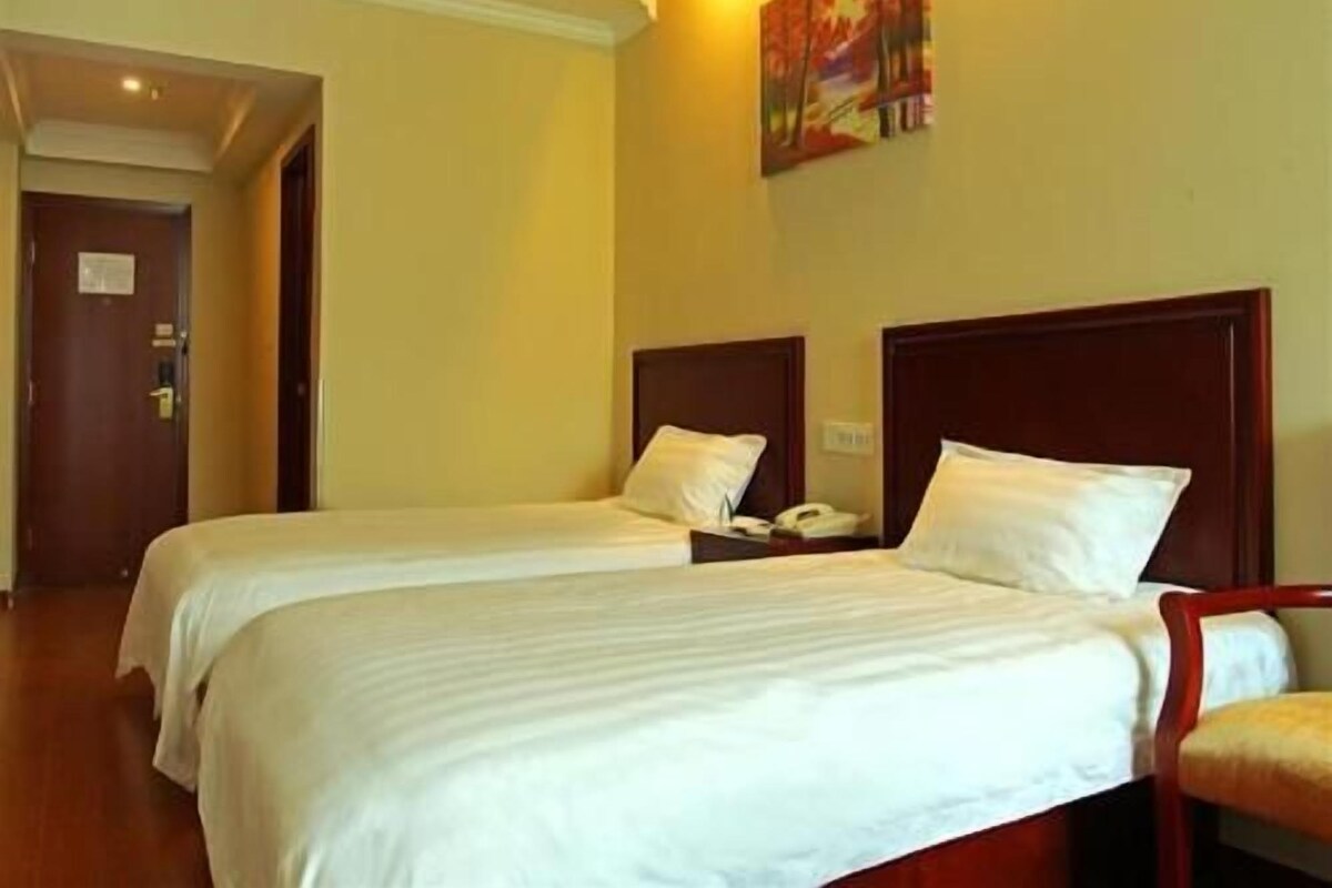 Quarto de hotel com duas camas, um quadro na parede e uma porta à esquerda.