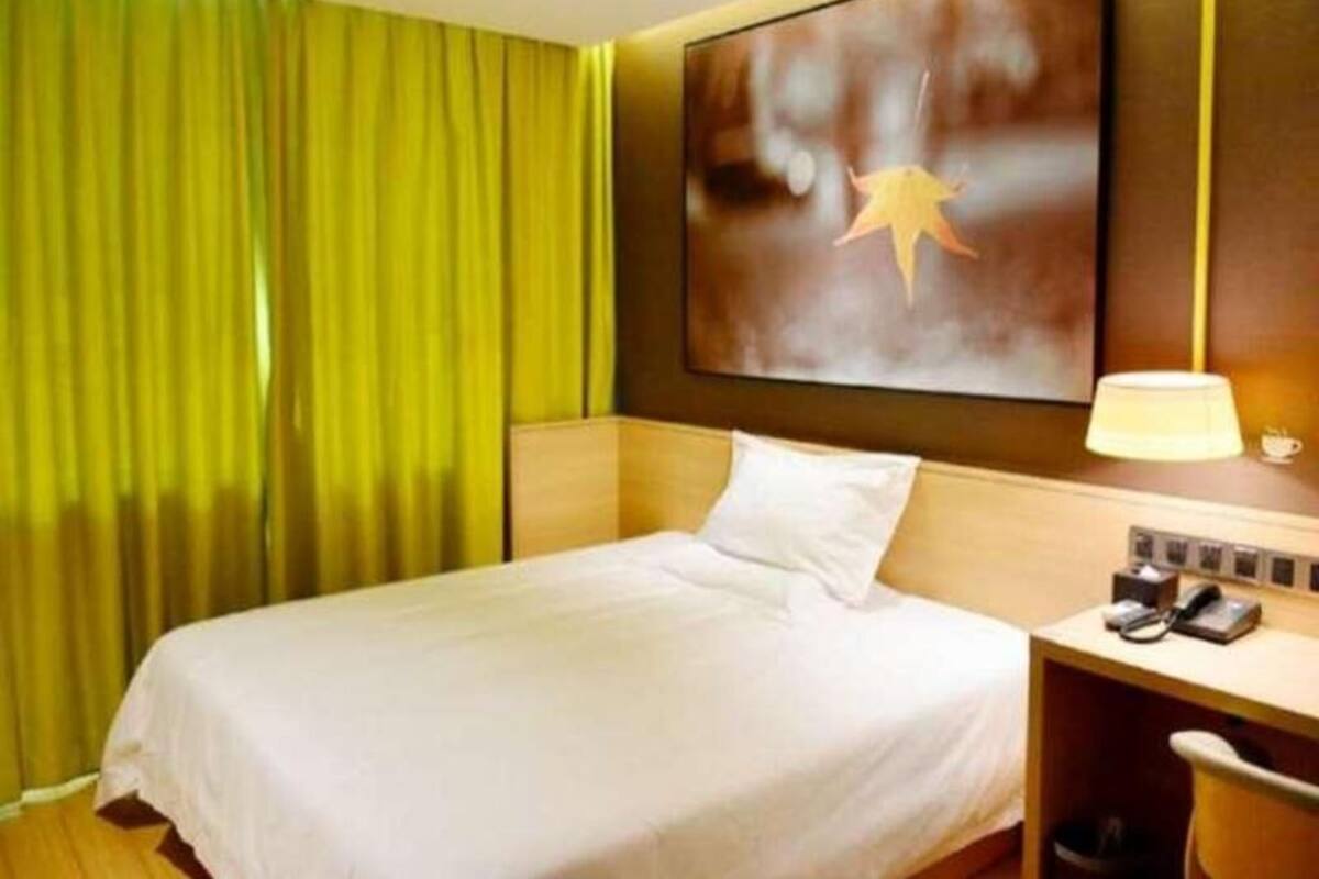 A hotel room with a bed, a desk with a lamp, a telephone, and a painting on the wall.