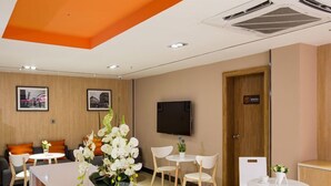 A reception area with a white reception desk, several chairs, a television mounted on the wall, and framed pictures on the wall. - IU Hotel (Taiyuan)