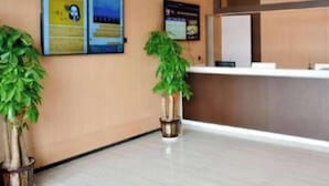 A reception area with a reception desk, two informational posters on the wall, and two potted plants. - IU Hotel (Taiyuan)
