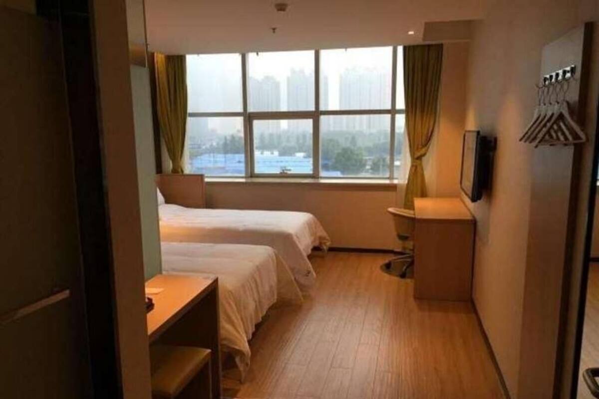 A hotel room with two beds, a desk, a chair, a TV, and a window with a view of buildings.