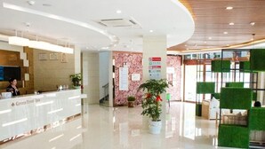 A hotel reception area with a reception desk, a potted plant, and a seating area with green cushions. - Greentree Inn (Huai'an)