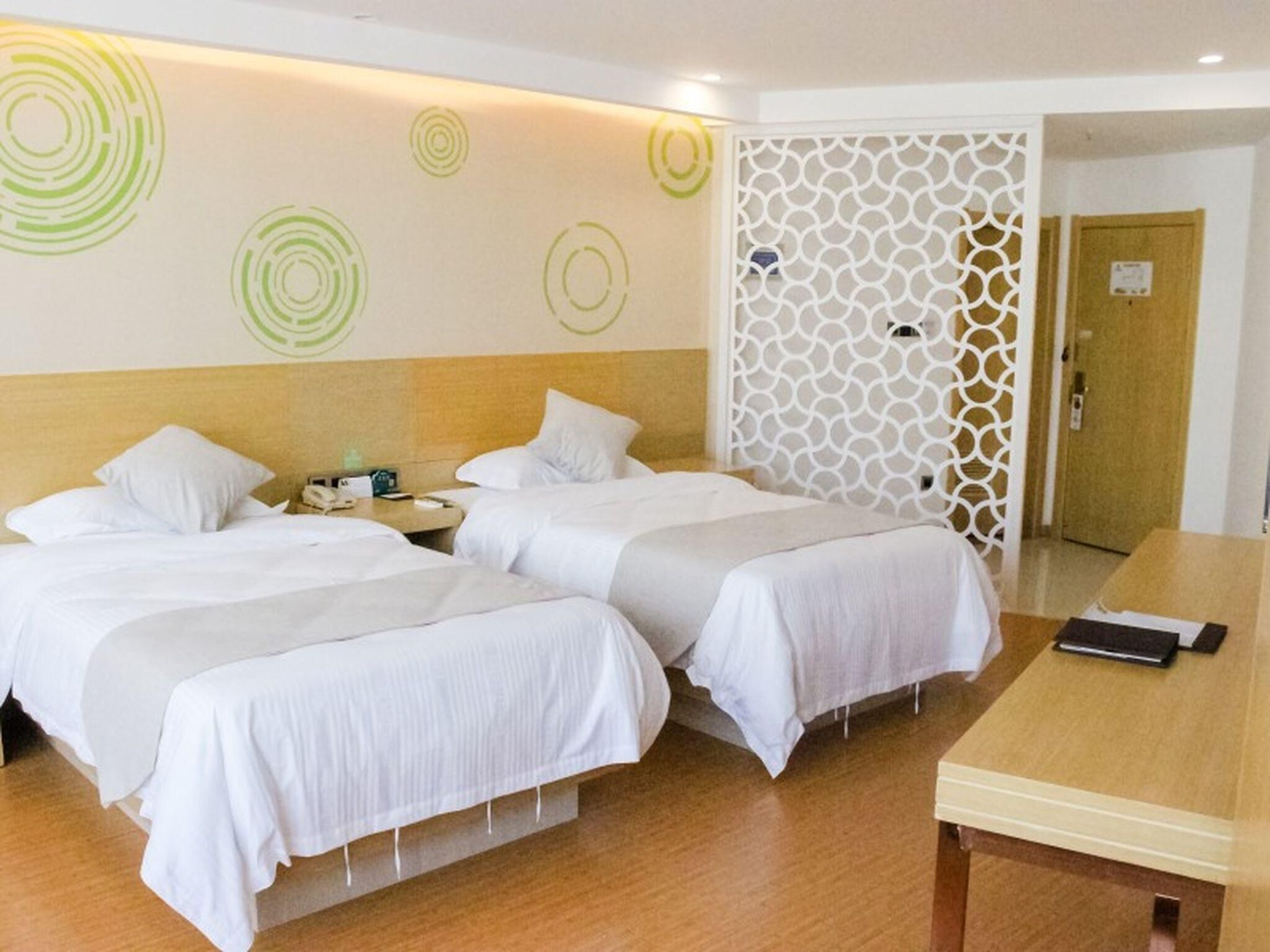 A hotel room with two beds, a wooden headboard, a white decorative wall panel, a wooden table, and a nightstand with a phone.