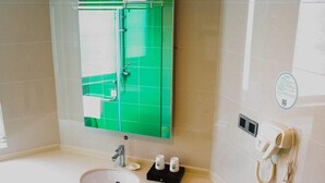 A bathroom with a green-tiled wall, a sink, a mirror, a hairdryer, and a small black tray with two bottles. - Greentree Inn (Huai'an)